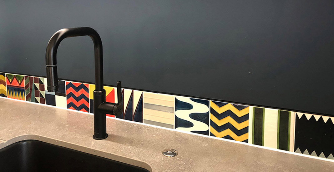 Single row multicoloured tile splash back in kitchen with a black tap and dark teal wall