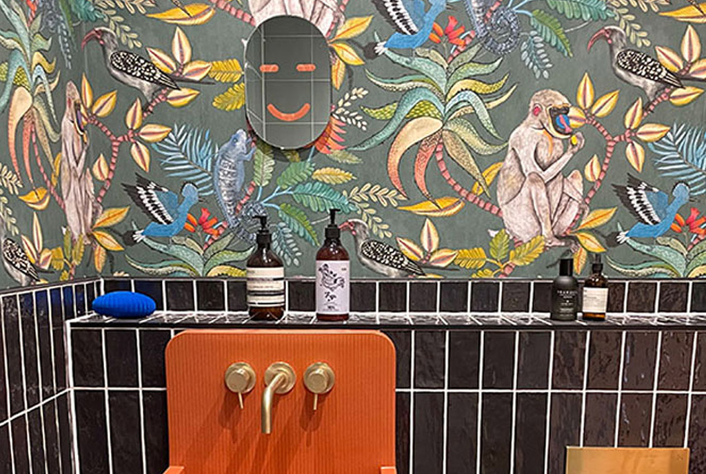 Orange concrete sink with gold taps, sits on vertical black gloss tiles with vibrate tropical and animal cole and sons savuti wallpaper cloakroom