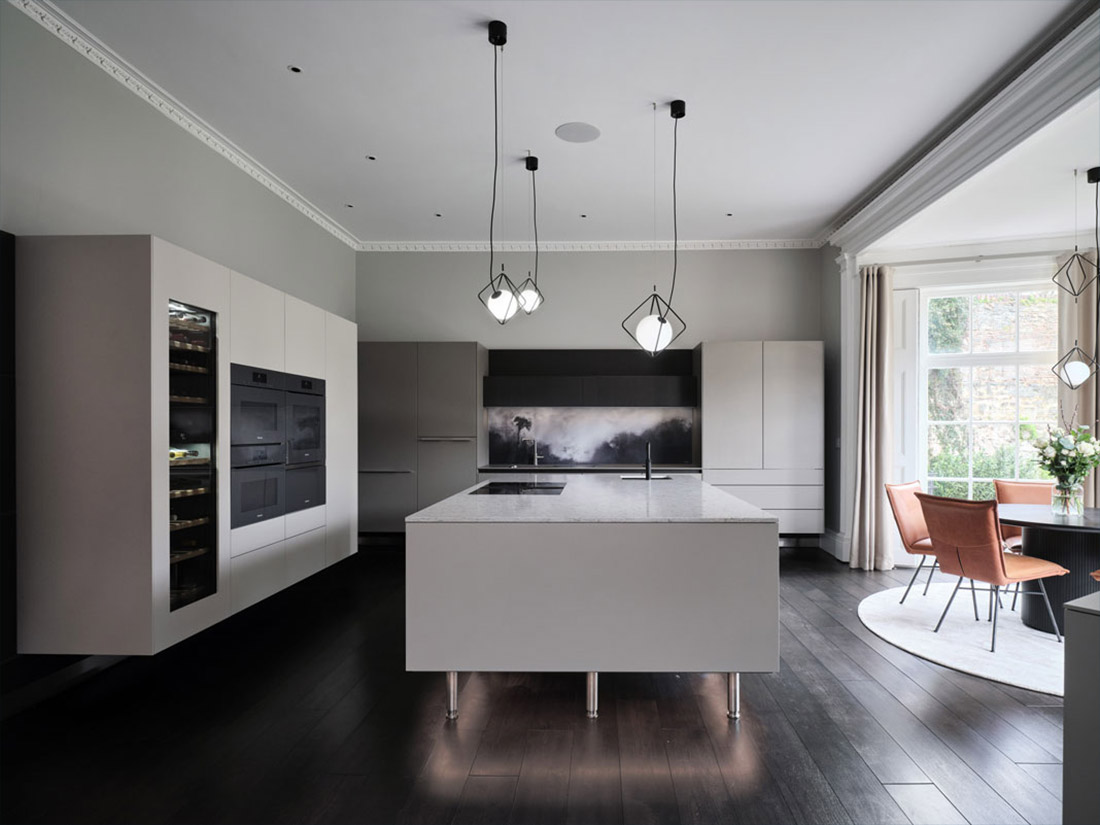Bultaup kitchen with art splashback with kitchen table and tan leather chairs to the right