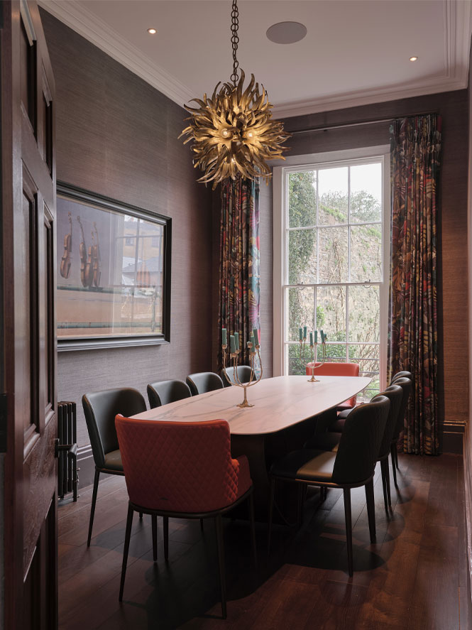 Dining room with dark wallpapered walls, gold chandeiler and colourful curtains