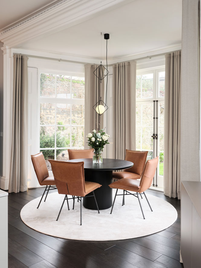 Kitchen-table-with-tan-leather-chairs sit in bay window with neutral curtains and rug