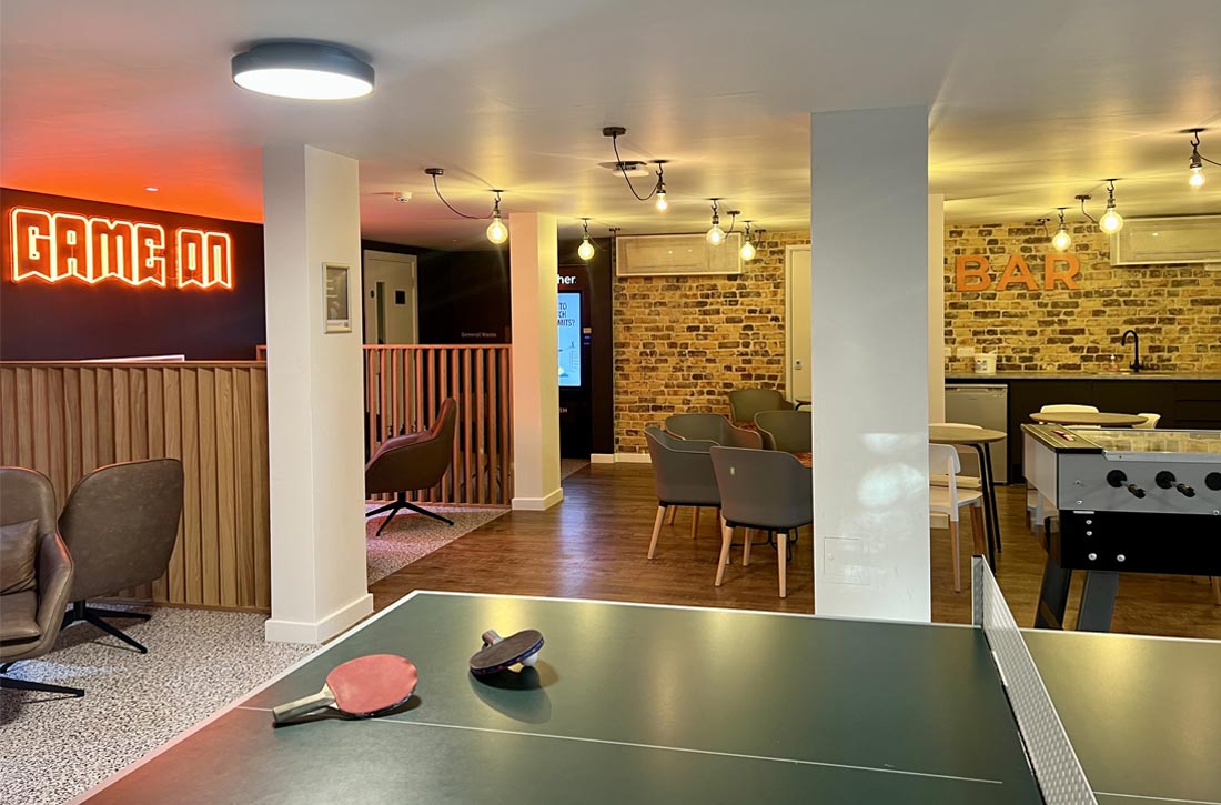 Student amenity space neon sign saying game on with a ping pong table and bar in background infront of abbrick all. Tuffnell Park joseph king interiors