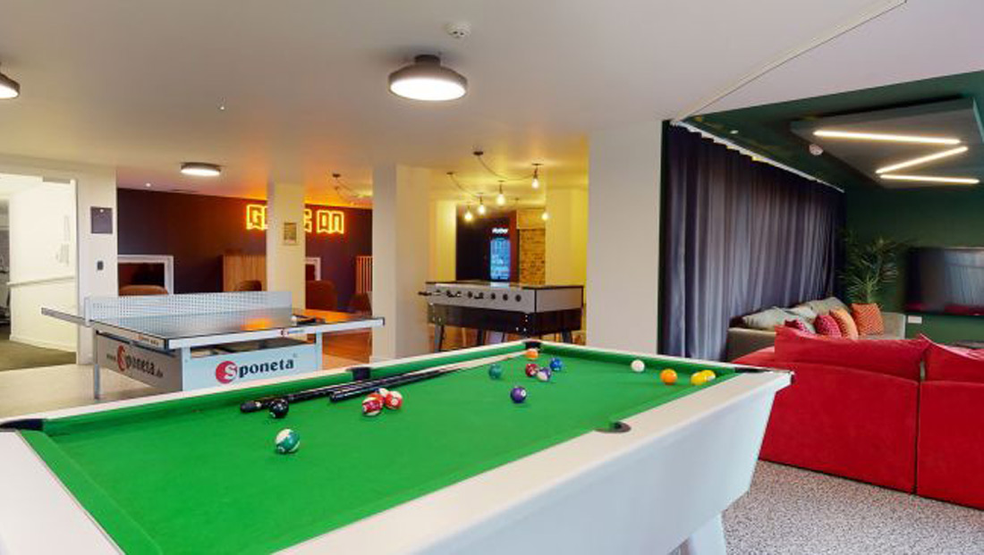Student amenity space showing pool table a red sofa in a cinema room with Game on sign in the back left.