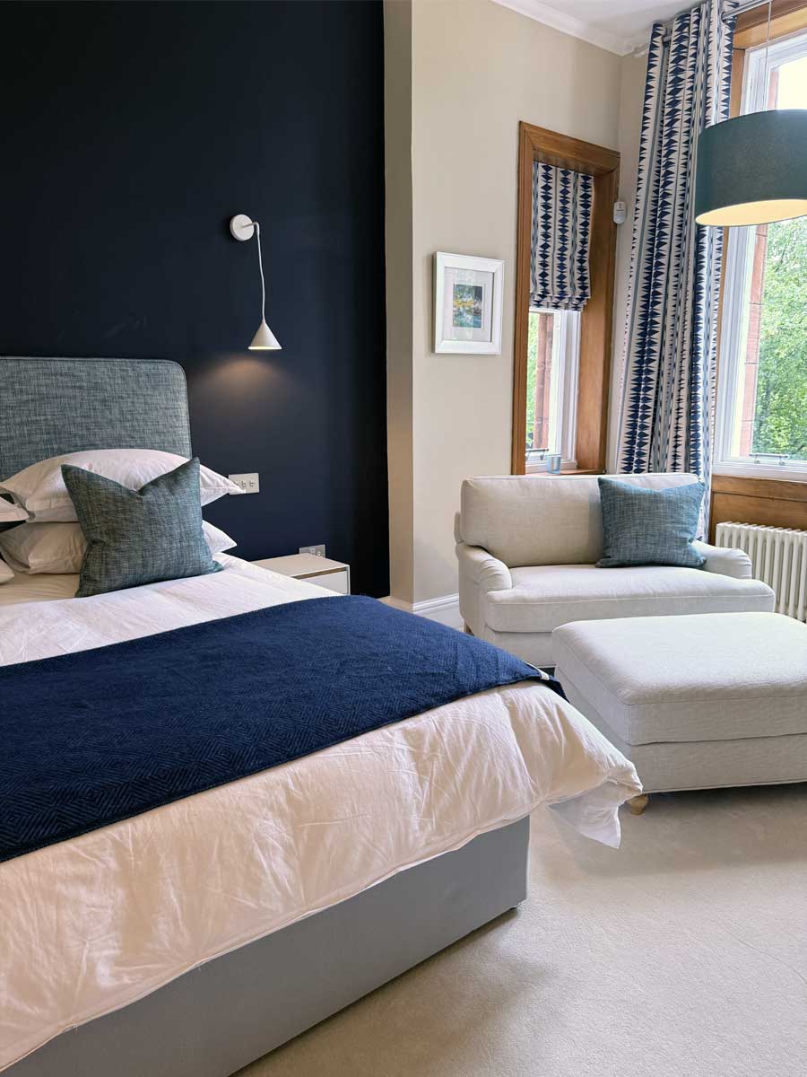 Dark blue accent wall luxury bedroom with off white chair to the side
